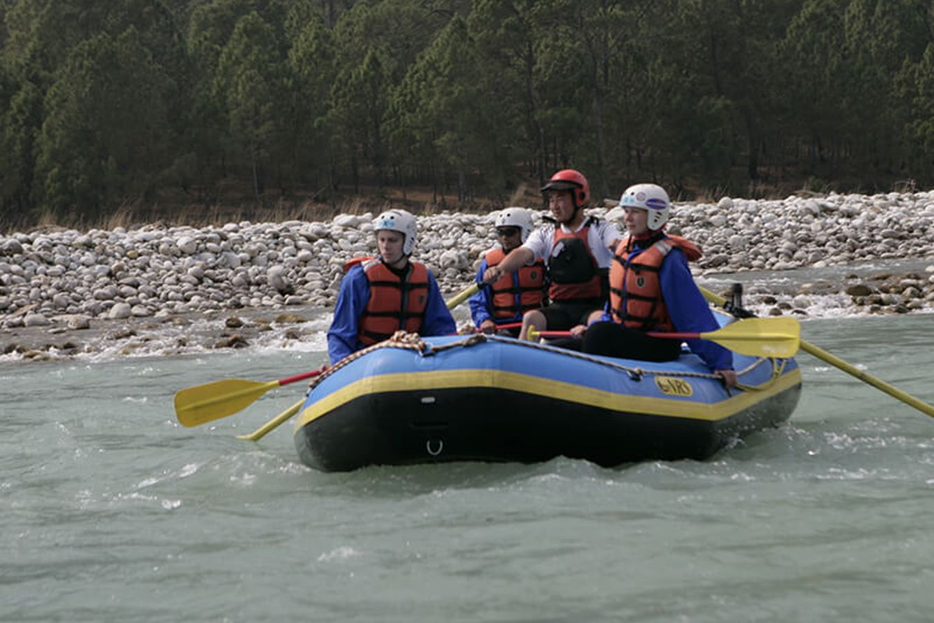 A raft of paddlers on a wide Bhutanese river between stony banks