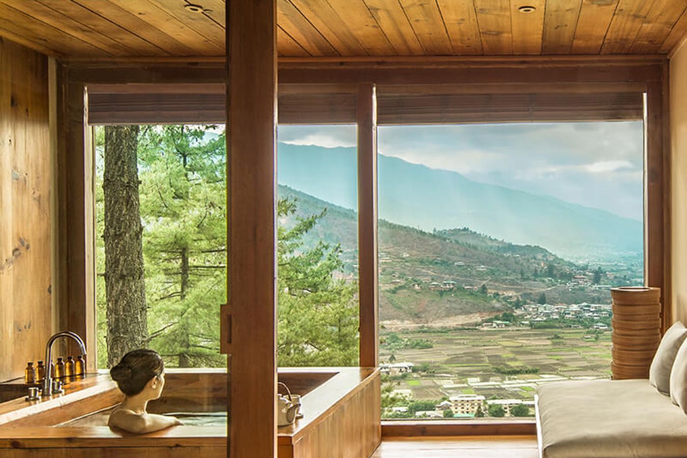 A timber bathhouse with a stone bath and windows open onto a Bhutanese valley
