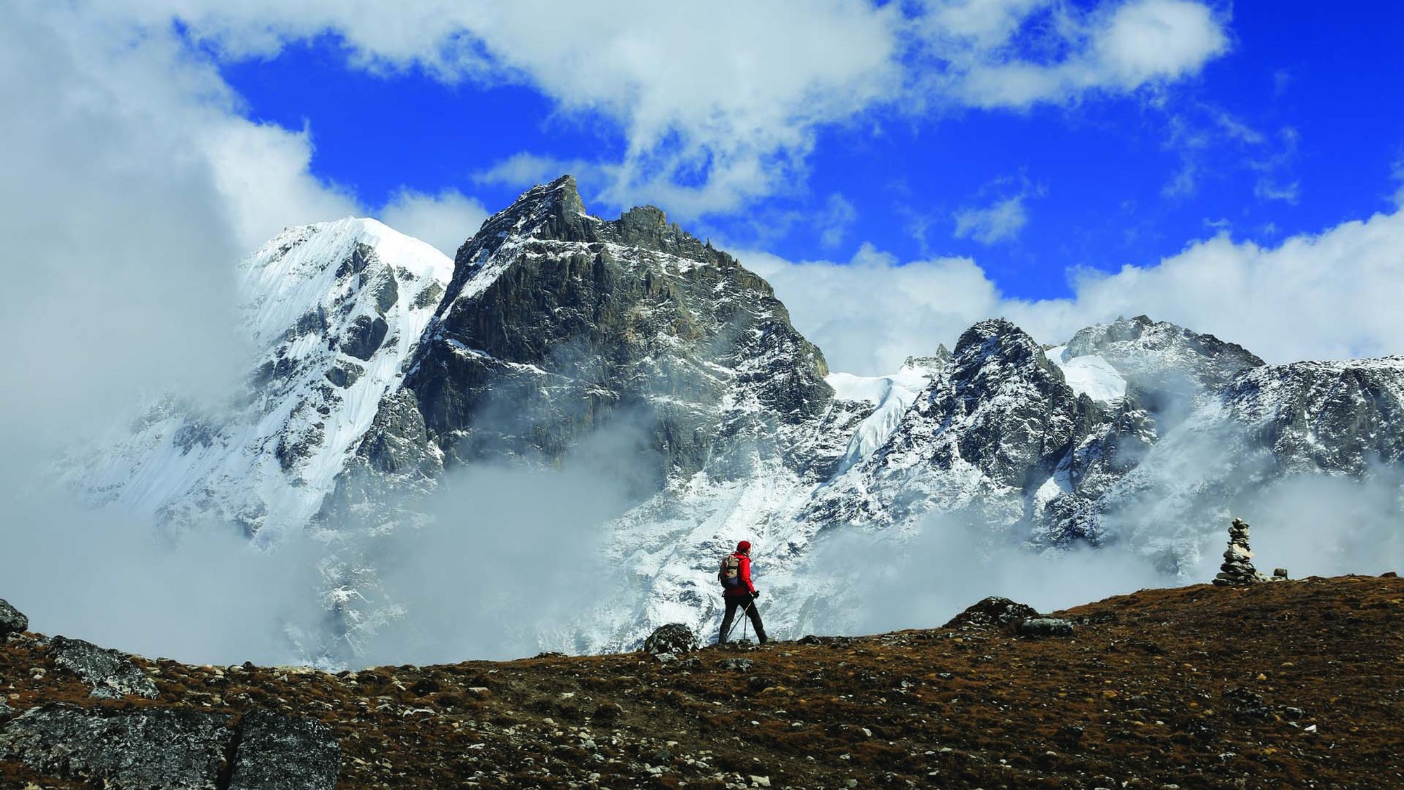 A lone trekker on a high ridge below snow-covered Himalayan peaks in northern Bhutan