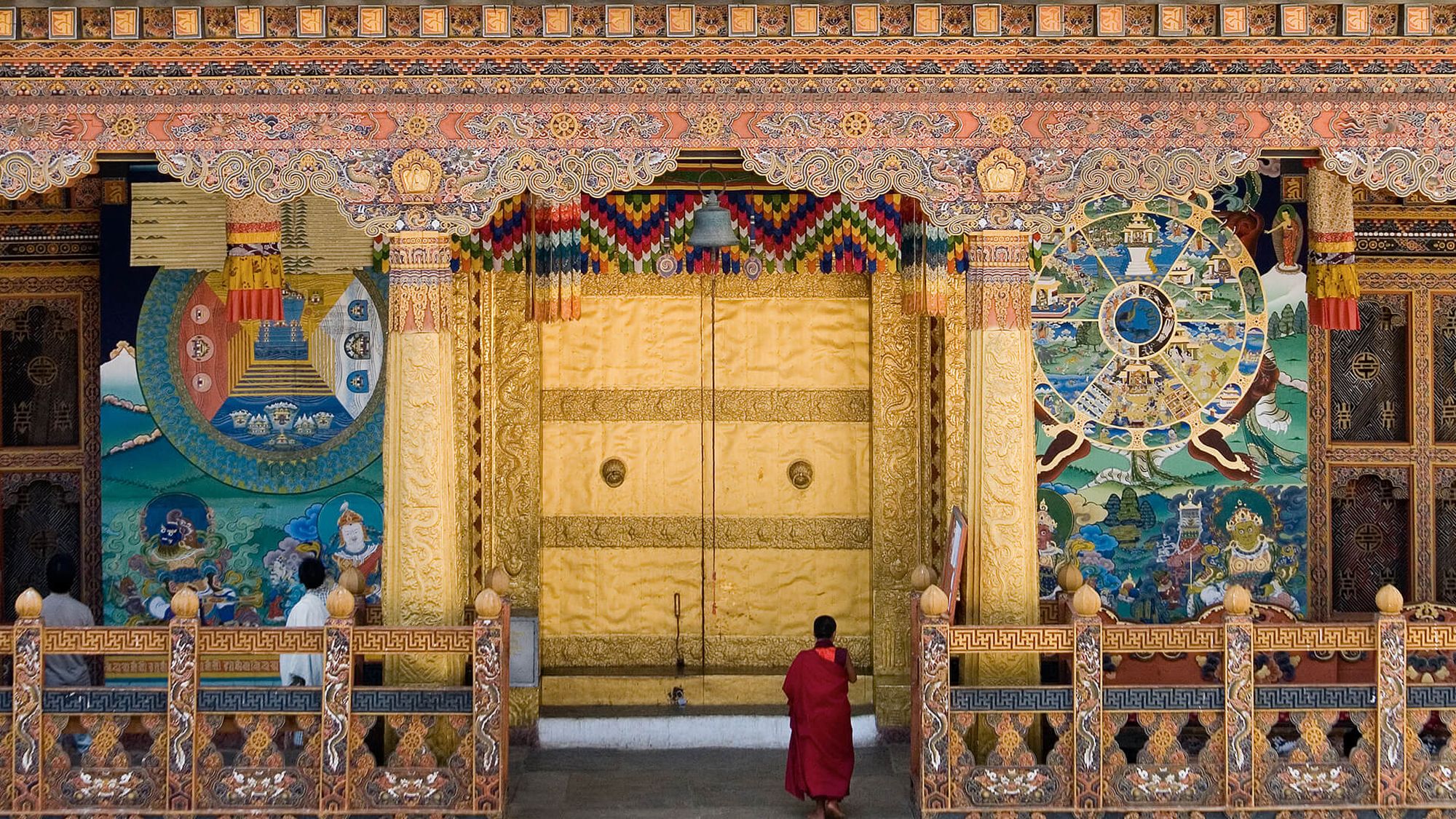 A young monk standing before the vast gilded doors of a Bhutanese temple