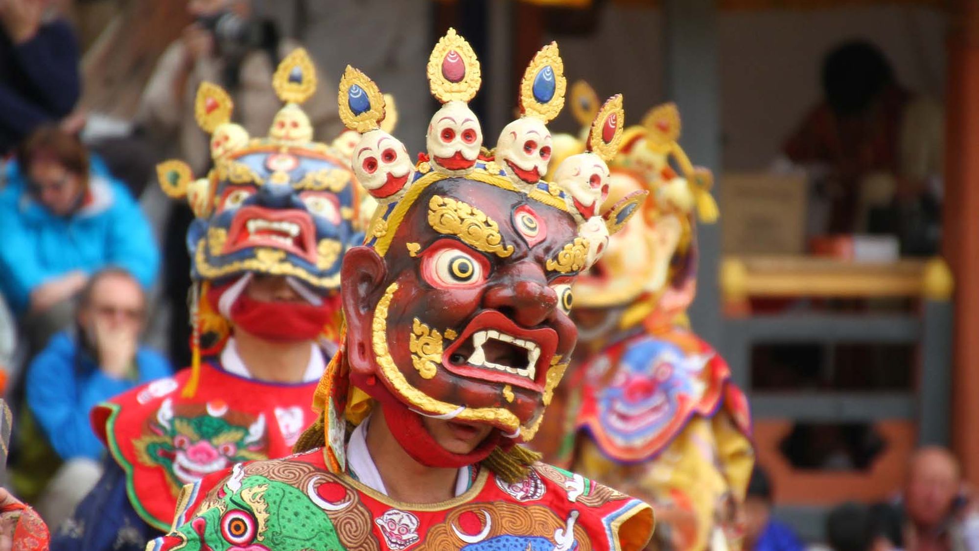 A masked cham dancer in a crowned headdress performing at the Thimphu Tshechu